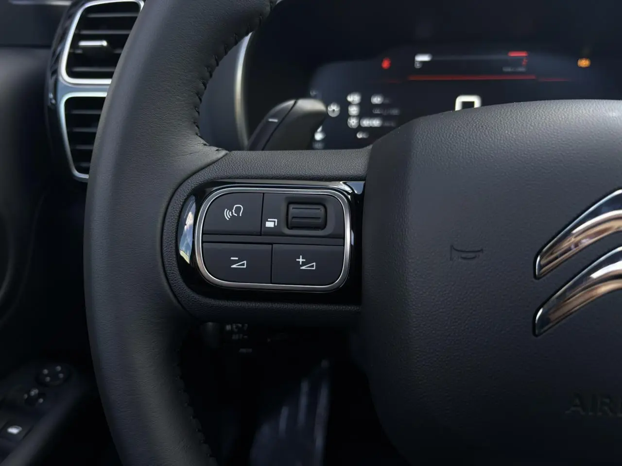 Gros plan sur les commandes gauche du volant cuir noir du Citroën C5 Aircross 2025, détails chromés et touches fonctionnelles.