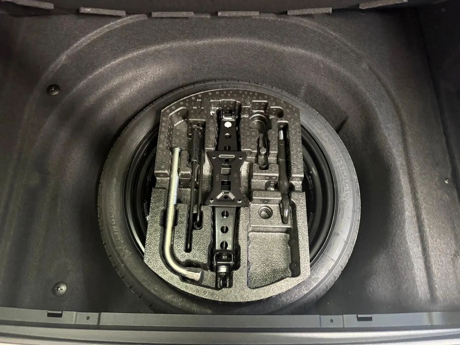 Vue plongeante sur la roue de secours et les outils de bord dans le coffre d'une Skoda Superb Combi gris argent 2025.