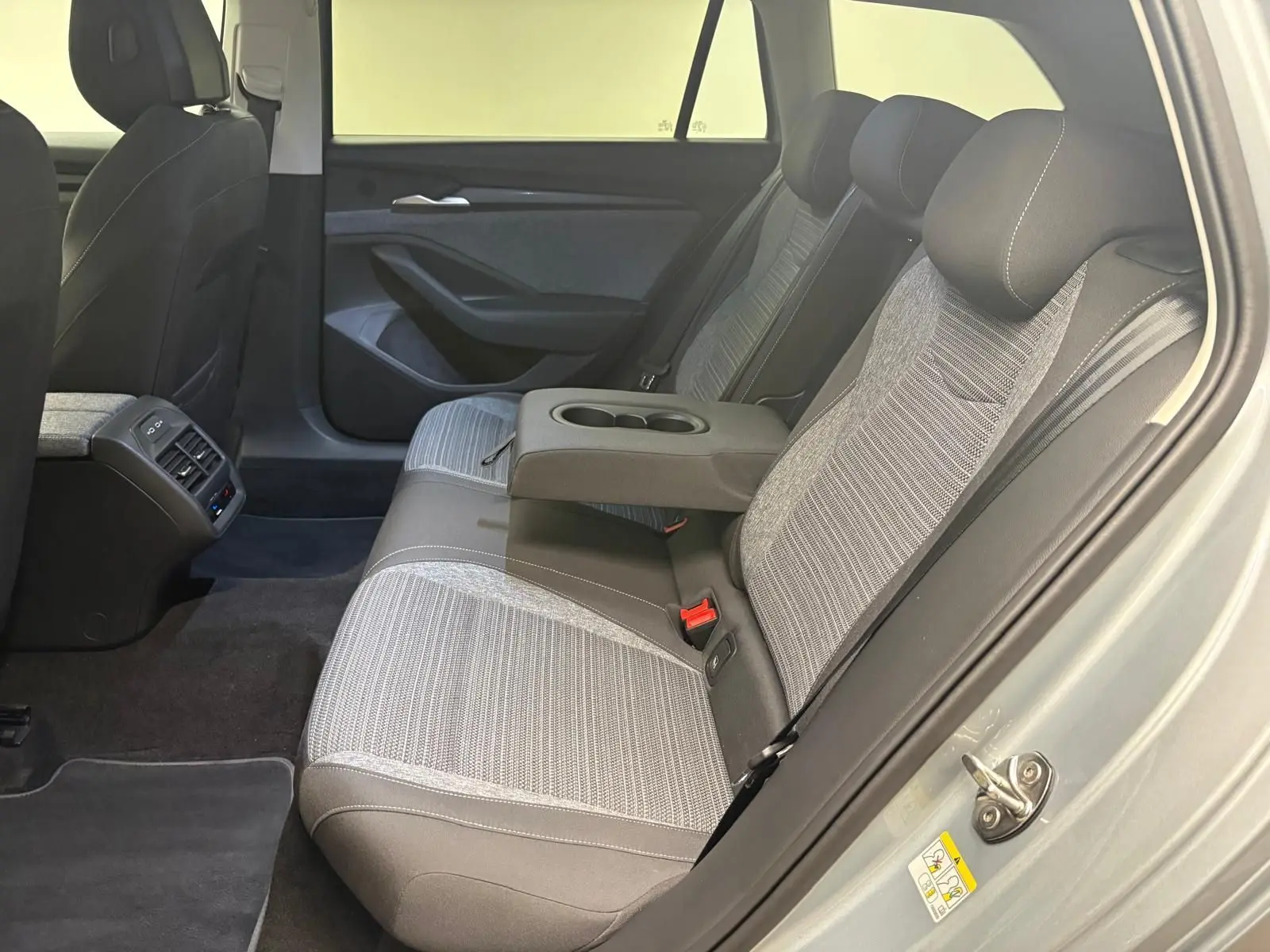 Vue intérieure côté droit des sièges arrière gris clair et foncé du Skoda Superb Combi 2025 avec accoudoir central relevé.