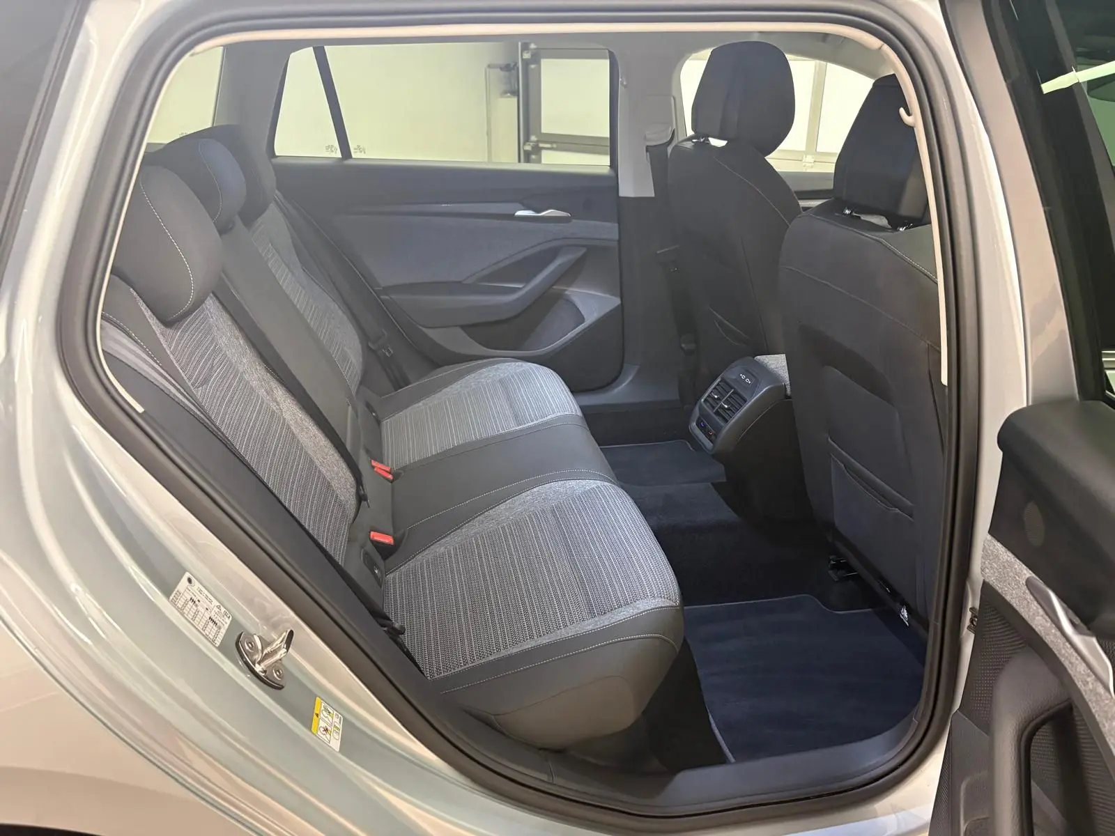 Vue intérieure côté arrière droit d'un Skoda Superb Combi gris argent 2025, montrant les sièges arrière et les aérations centrales.