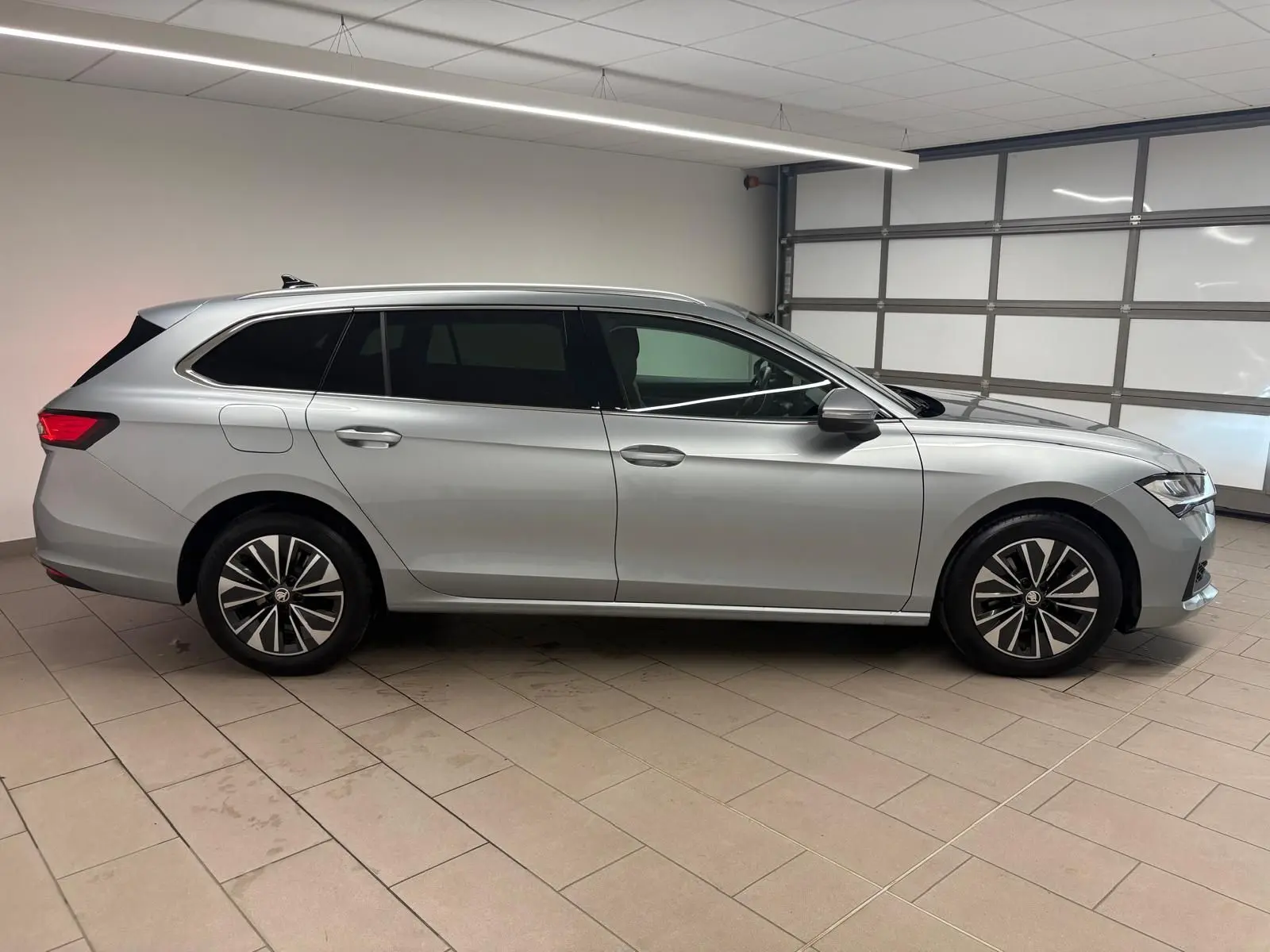 Vue latérale droite d'une Skoda Superb Combi gris argent 2025 dans un garage, avec jantes alliage distinctives.