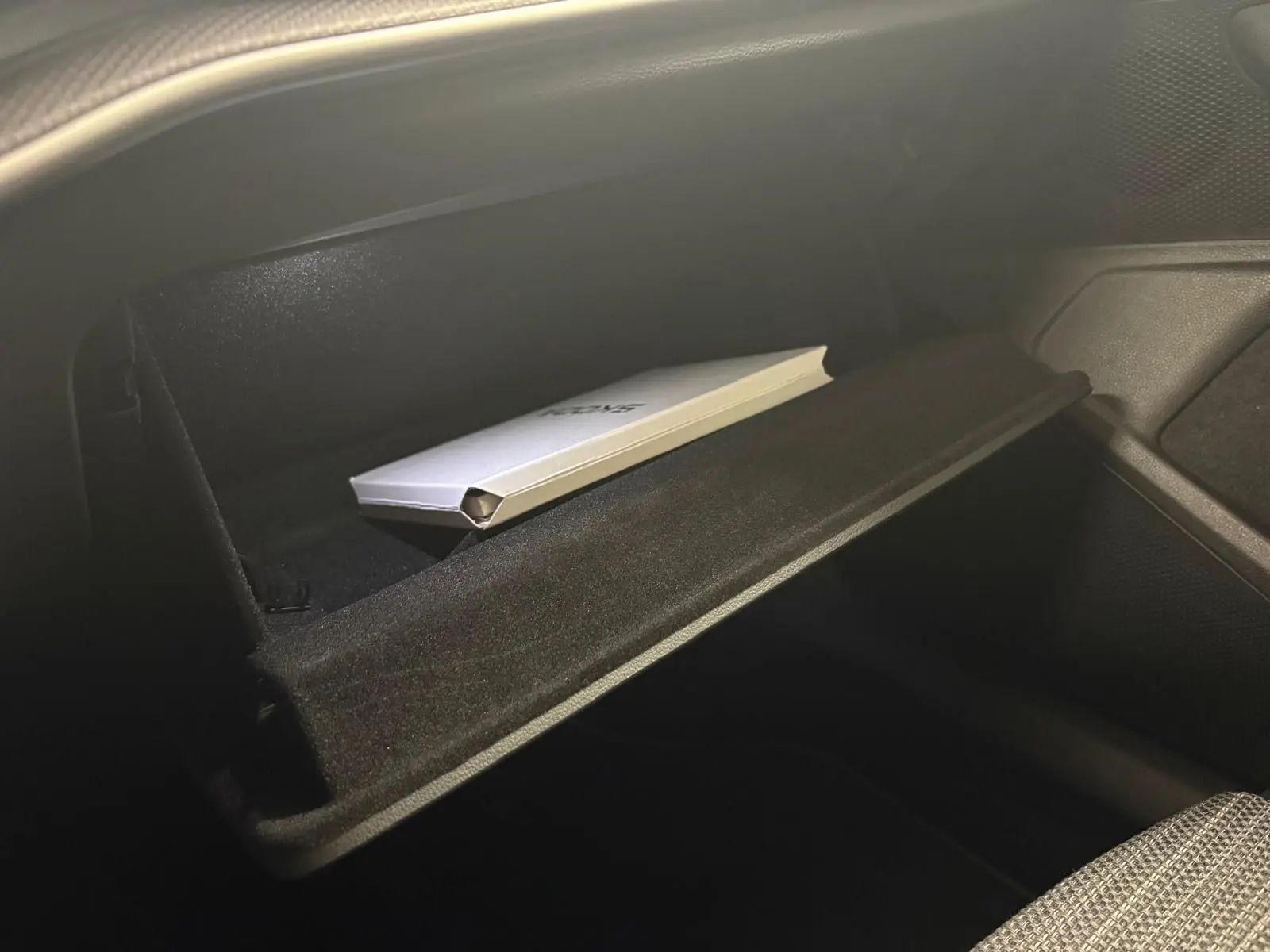 Gros plan sur la boîte à gants ouverte du Skoda Superb Combi gris argent 2025, avec un manuel à l'intérieur.