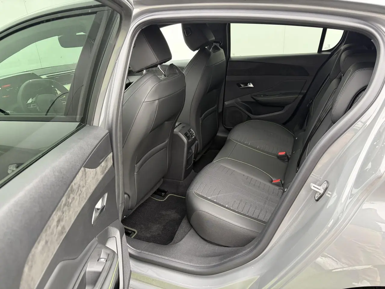 Vue côté gauche arrière de l’habitacle gris d’une Peugeot 308 III hybride avec sièges noirs et surpiqûres vert Adamite.