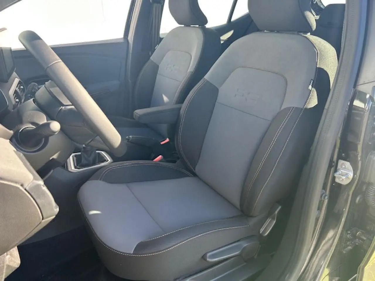 Vue intérieure côté conducteur de la Dacia Sandero III Stepway 2025, sièges gris et noir nacré avec accoudoir.