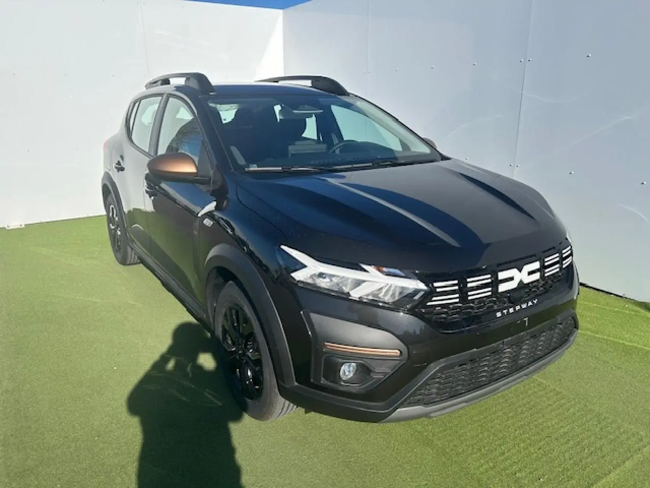 Dacia Sandero III Stepway noir nacré vue 3/4 avant droit avec calandre et barres de toit brun cuivré.