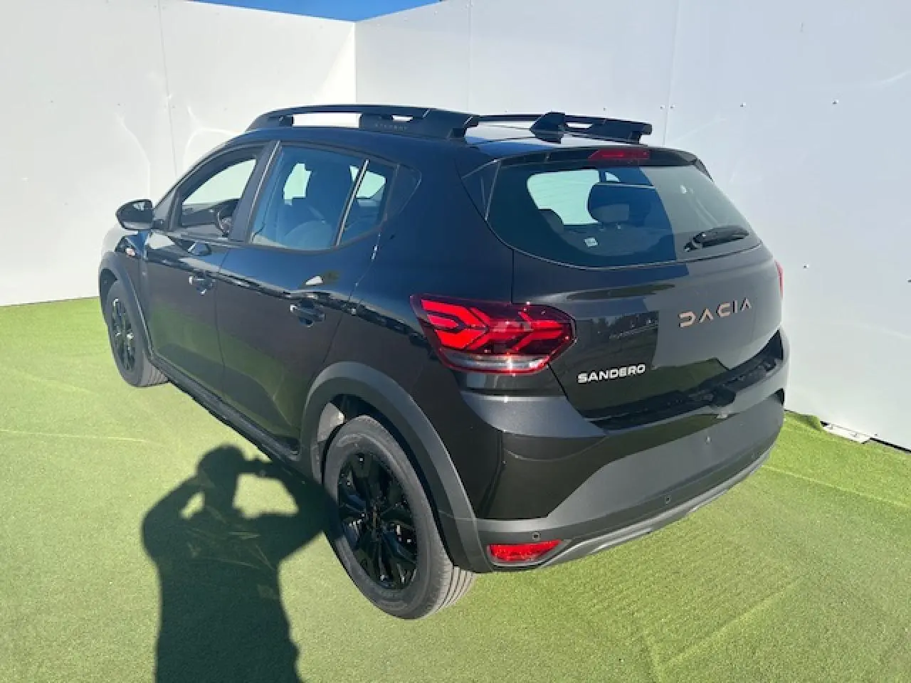 Vue 3/4 arrière droite d'une Dacia Sandero III Stepway noire nacrée avec jantes noires et barres de toit.