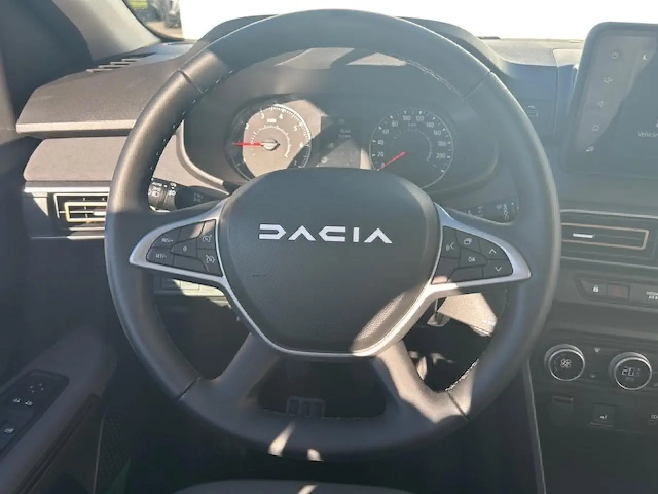 Vue intérieure centrée sur le volant noir du Dacia Sandero III Stepway avec tableau de bord et commandes visibles.
