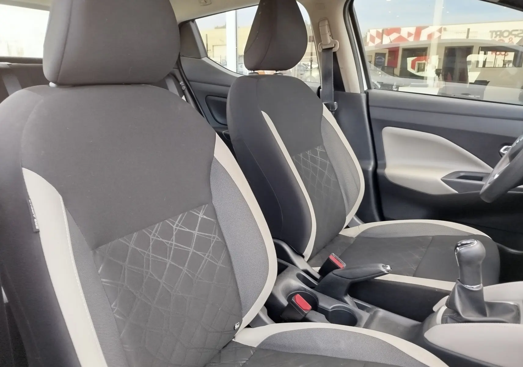 Vue intérieure côté conducteur de la Nissan Micra blanche 2019, sièges tissu gris et console avec levier de vitesse manuel.