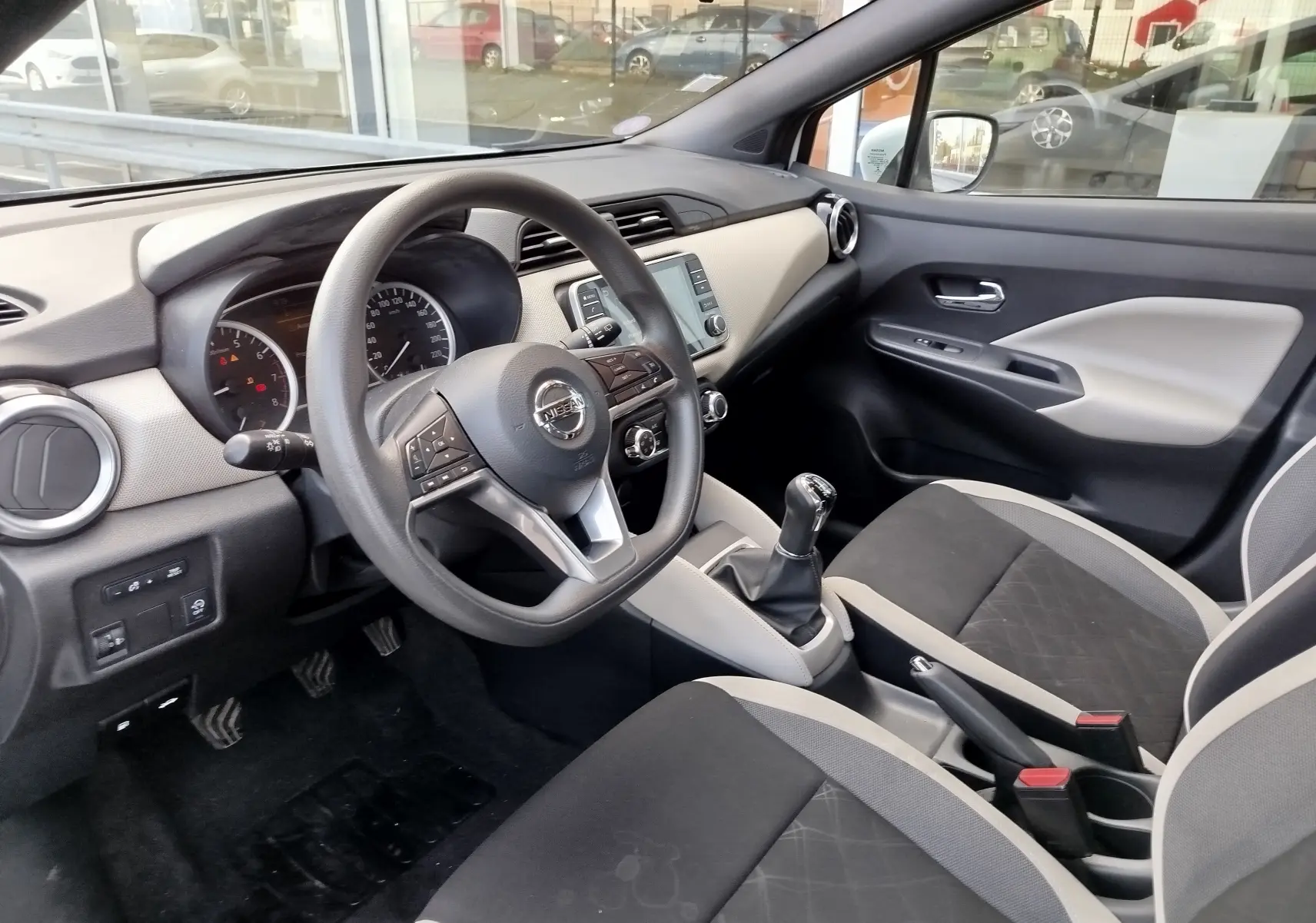 Vue intérieure côté conducteur de la Nissan Micra blanche 2019 avec volant multifonction et sellerie bicolore gris noir.