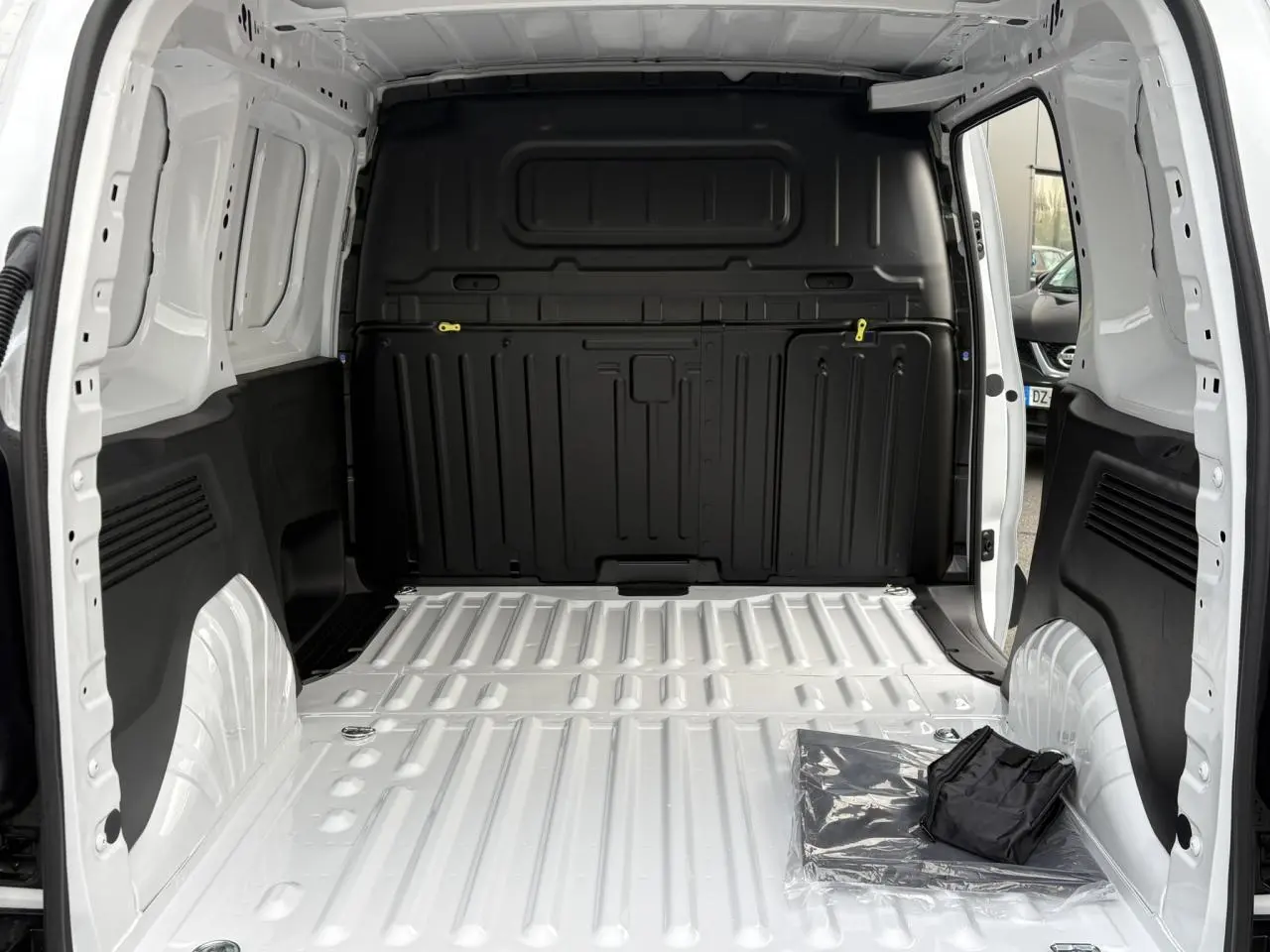 Vue intérieure de la zone de chargement blanche du Citroën Berlingo Van 2025 avec cloison noire et porte latérale ouverte.