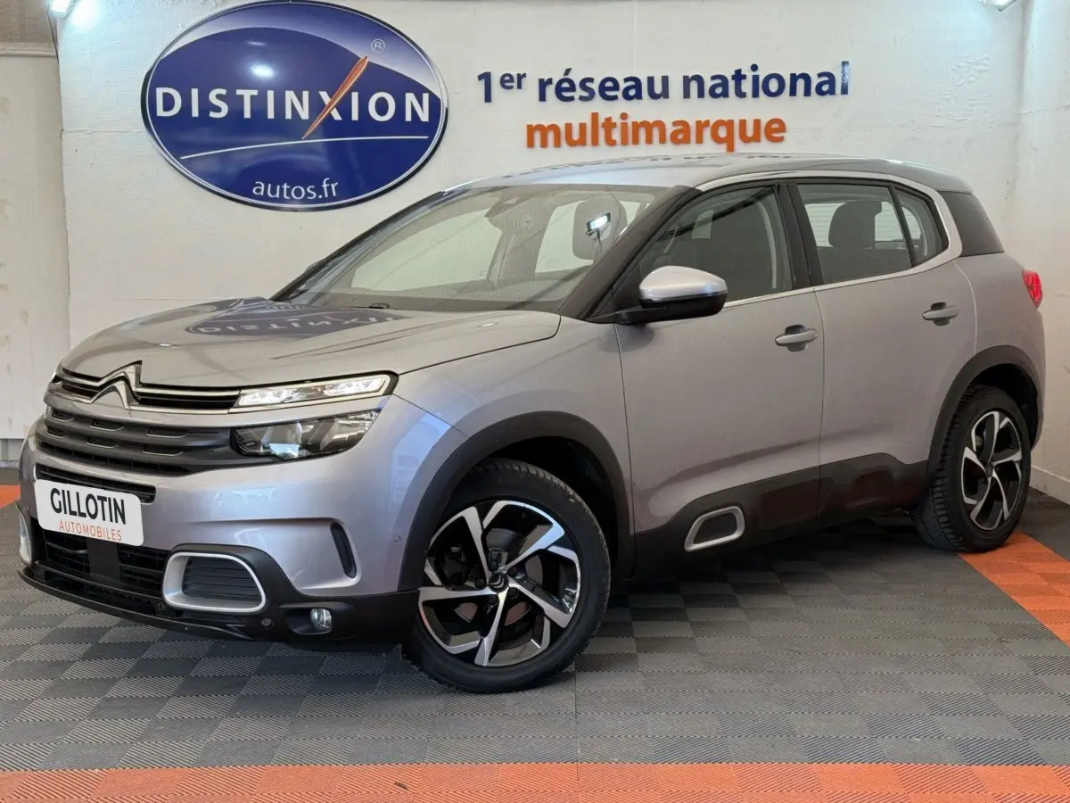 Citroën C5 Aircross gris clair en 3/4 avant droit, avec jantes noires et détails noirs sur les bas de caisse.