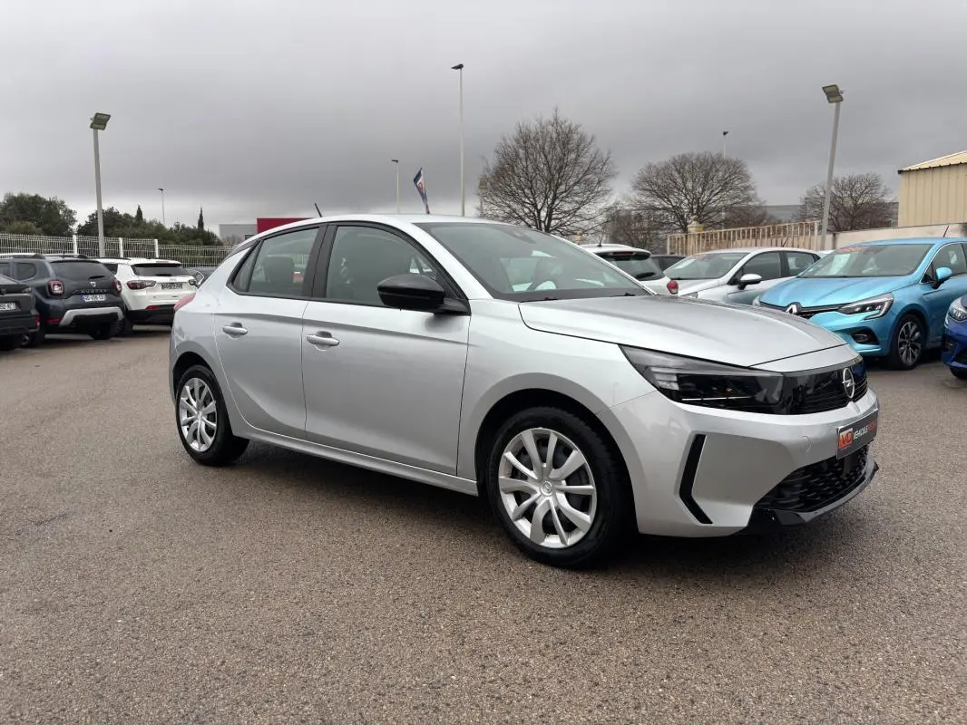 Opel Corsa gris clair vue 3/4 avant droit, avec jantes classiques et rétroviseurs noirs contrastants.