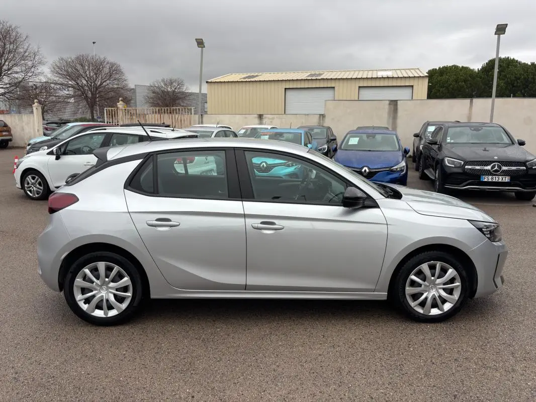 Vue latérale droite d'une Opel Corsa gris clair 2024 avec jantes classiques, garée en extérieur sur un parking.
