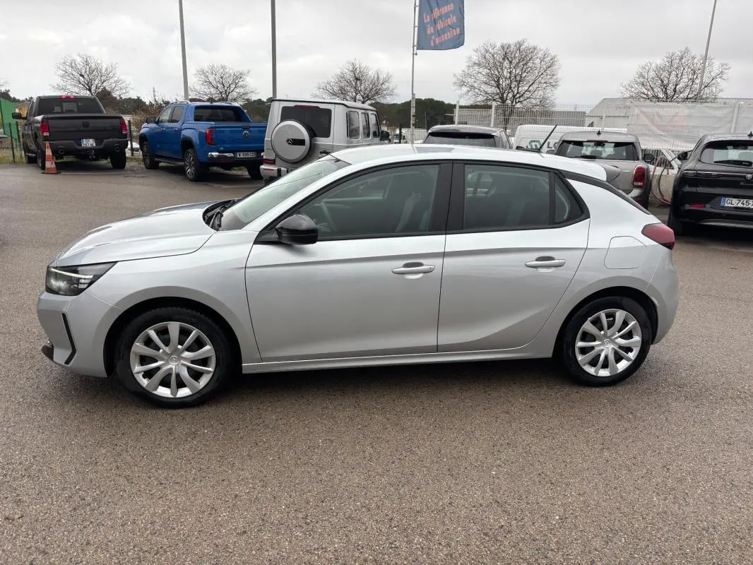 Opel Corsa gris clair vue de profil côté gauche, avec jantes classiques et rétroviseurs noirs.