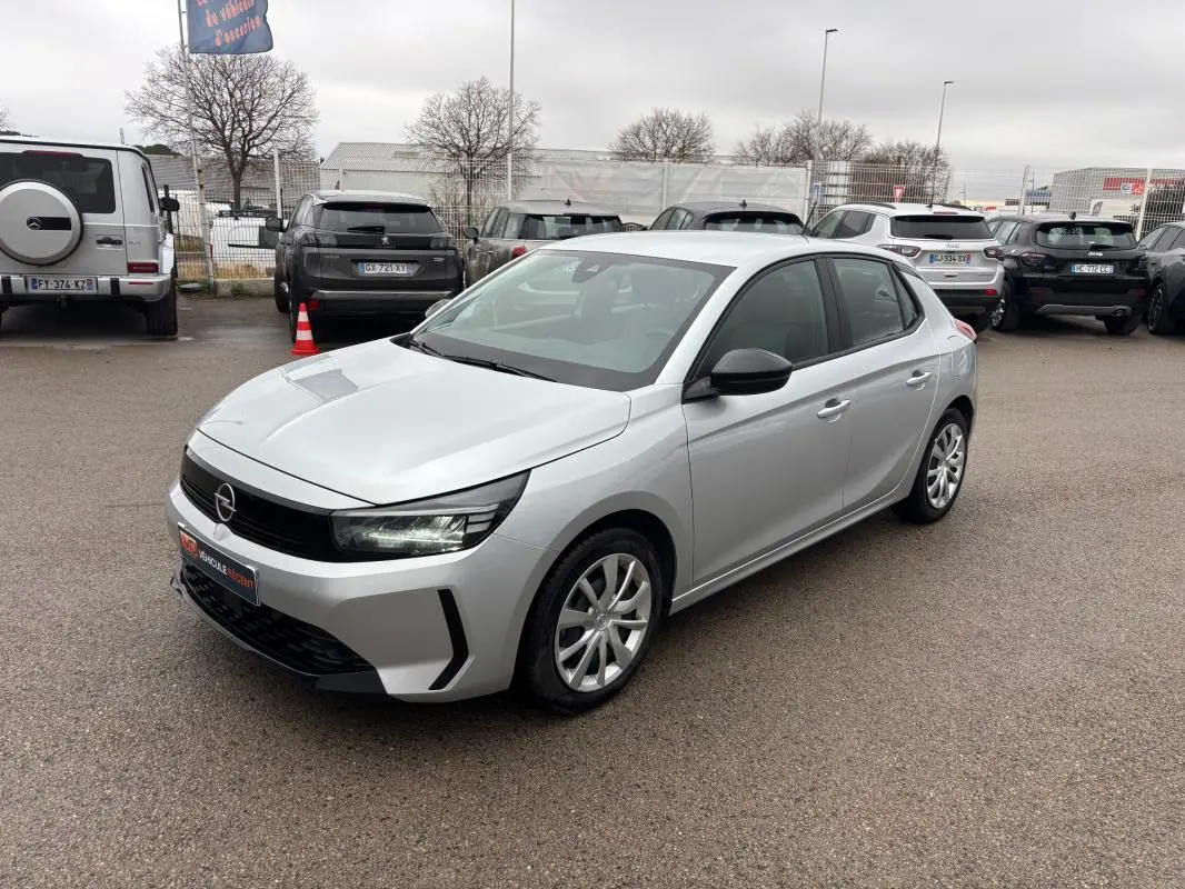 Opel Corsa gris clair vue 3/4 avant droit, avec jantes classiques et rétroviseurs noirs contrastants.