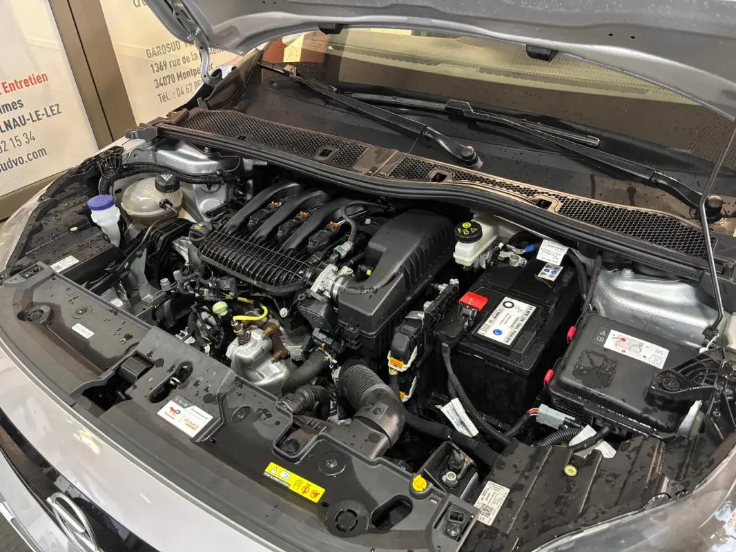 Moteur essence de l’Opel Corsa gris clair 2024 vu de face avec capot ouvert, batterie et composants visibles.