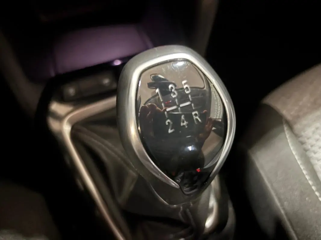 Gros plan sur le levier de vitesses manuel noir et chrome de l’Opel Corsa gris clair, intérieur sombre.