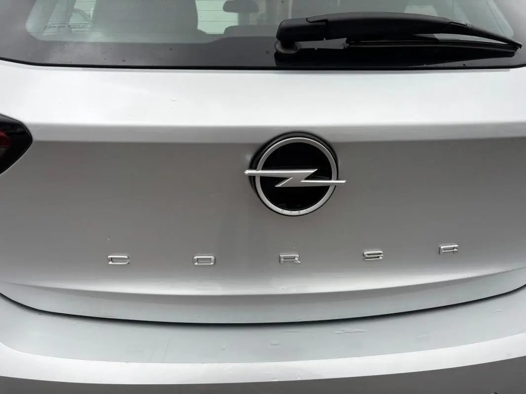 Gros plan sur le logo Opel et l'inscription Corsa à l'arrière d'une voiture gris clair.