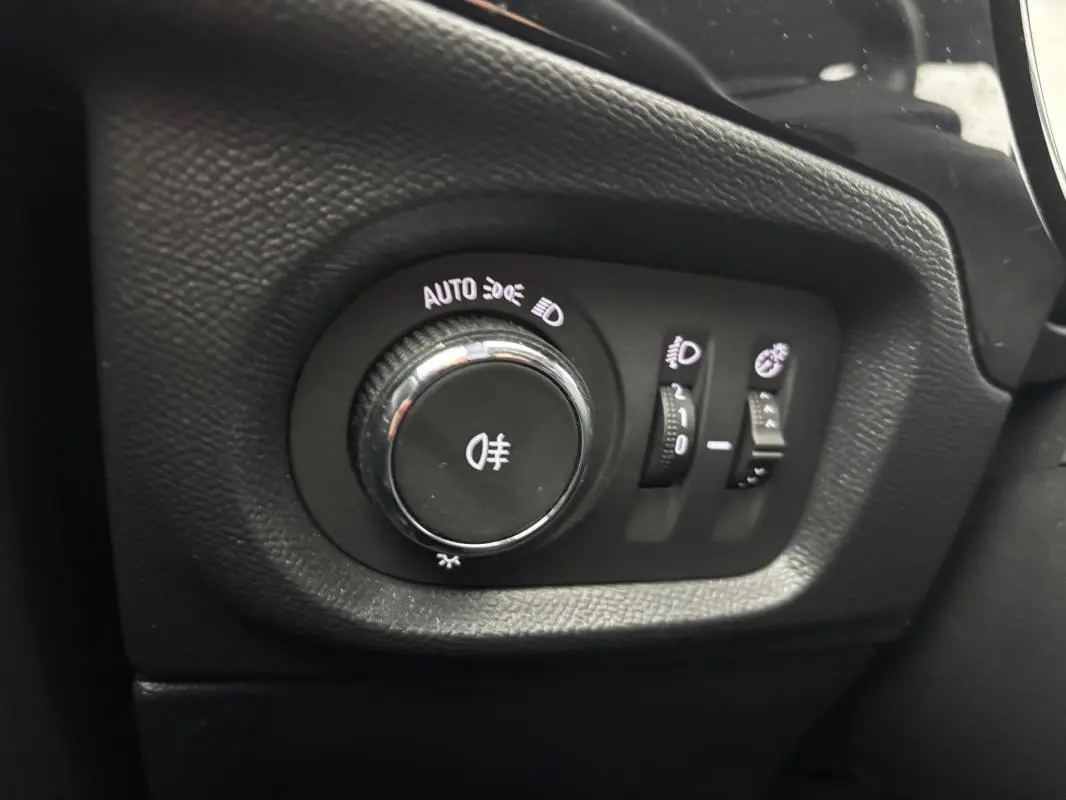 Gros plan sur le bouton de commande des feux avec réglages automatiques dans l’habitacle noir de l’Opel Corsa gris clair.