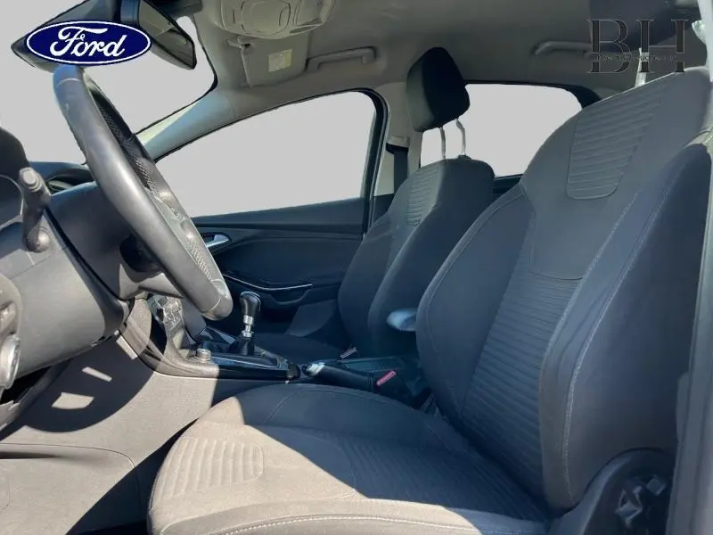 Vue intérieure côté conducteur de la Ford Focus 1.0 EcoBoost 2017 avec sièges sport en tissu noir et volant cuir multifonction.