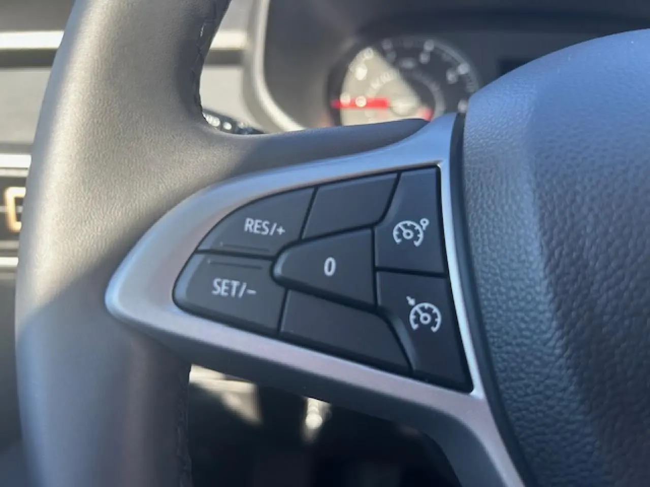 Gros plan sur les commandes du régulateur de vitesse au volant noir du Dacia Sandero III Stepway beige Safari.