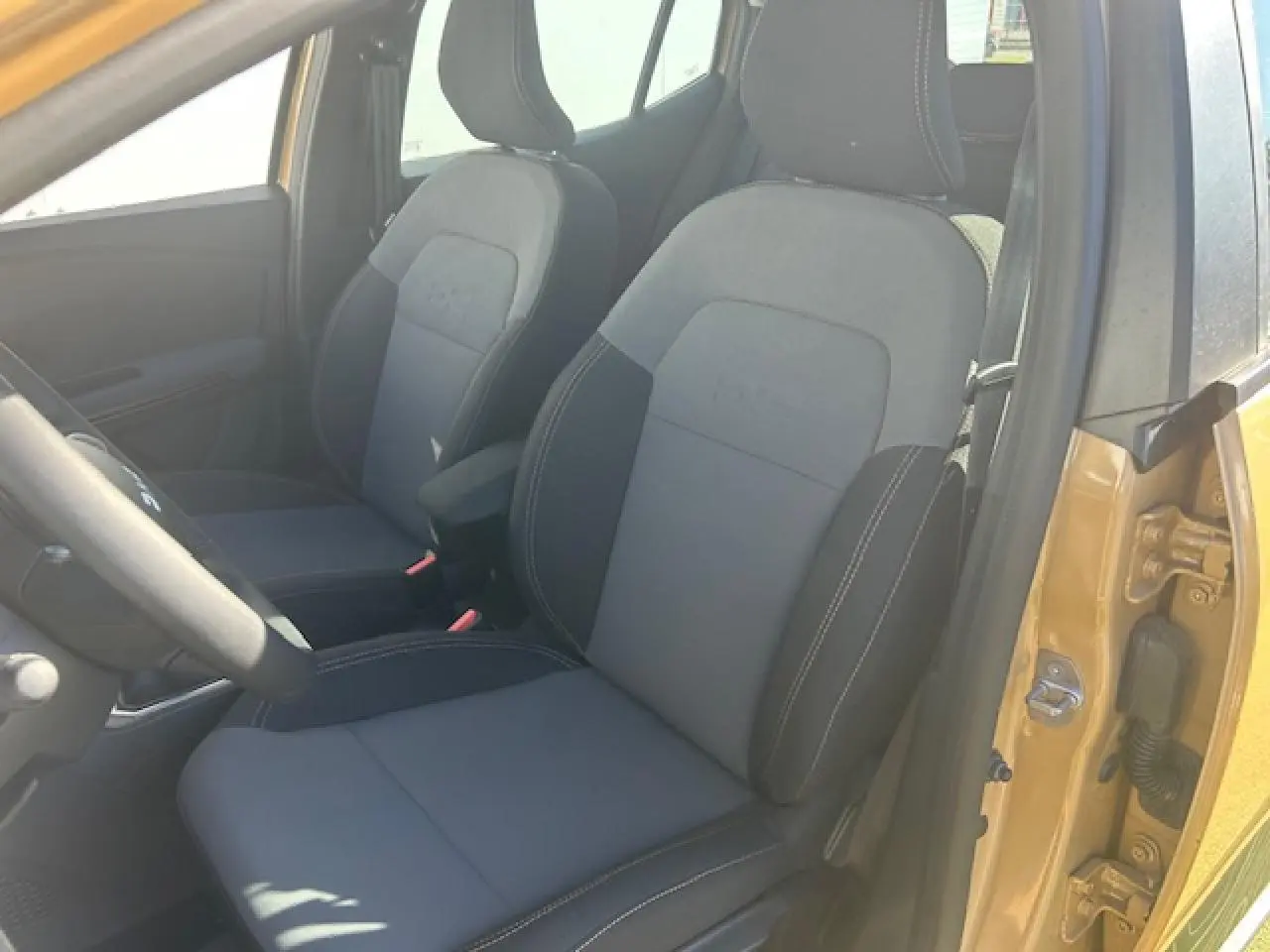 Vue intérieure côté conducteur de la Dacia Sandero III Stepway beige Safari, avec sièges noirs et accoudoir central.