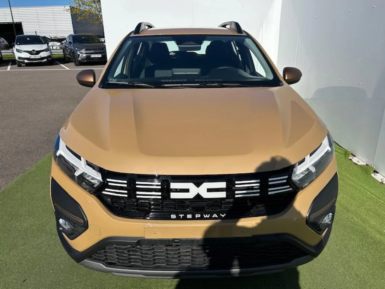 Vue avant rapprochée d'une Dacia Sandero Stepway beige Safari avec calandre noire et logo central distinctif.