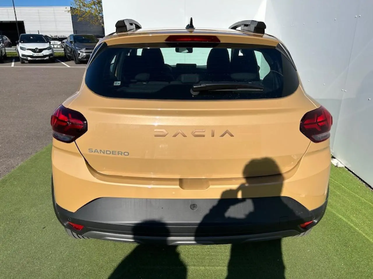 Vue arrière d'une Dacia Sandero beige Safari avec logo et feux arrière LED visibles sur fond extérieur.