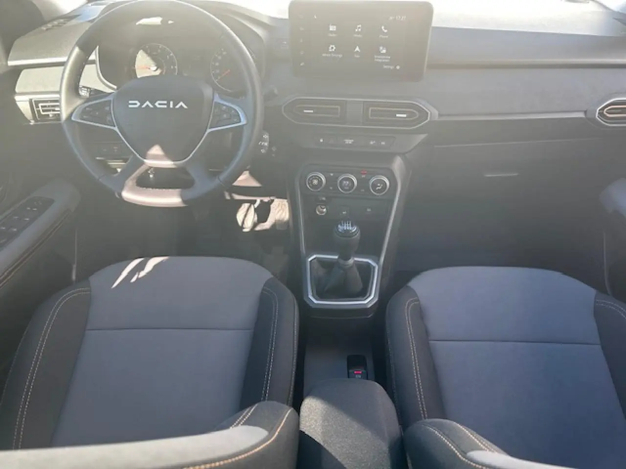 Vue intérieure avant de la Dacia Sandero III Stepway, tableau de bord noir avec écran tactile et volant multifonction.