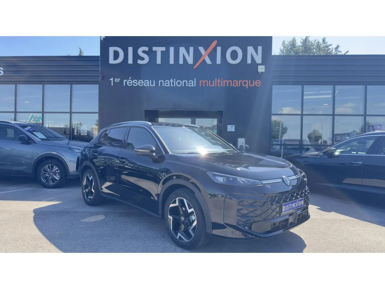 Volkswagen T-Roc noir en 3/4 avant droit, avec jantes stylisées et toit panoramique visible au soleil.
