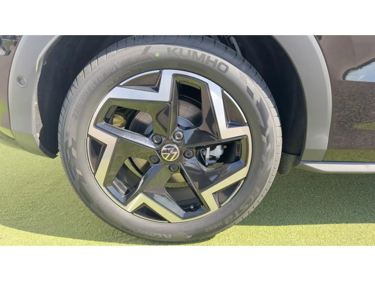 Gros plan sur la roue avant droite du Volkswagen T-Roc noir avec jante 18 pouces bicolore et logo VW au centre.