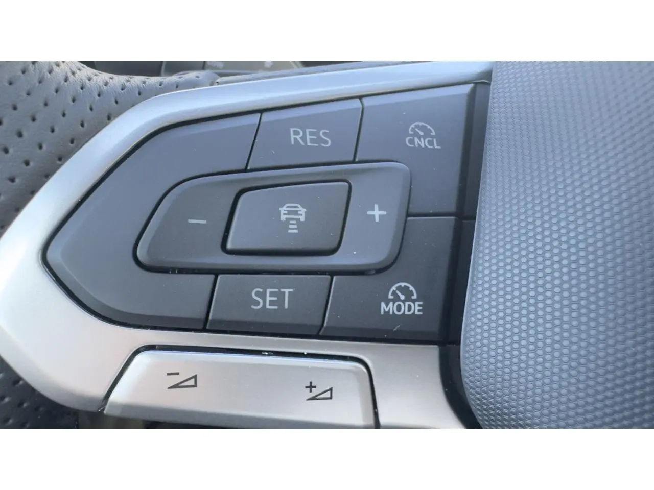 Gros plan sur les commandes du régulateur de vitesse au volant cuir perforé du Volkswagen T-Roc noir, version R-Line.