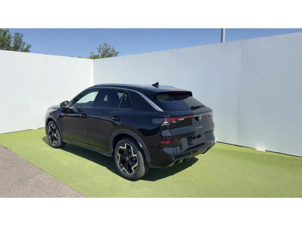 Volkswagen T-Roc noir en 3/4 arrière droit, avec jantes noires et toit ouvrant panoramique visible.