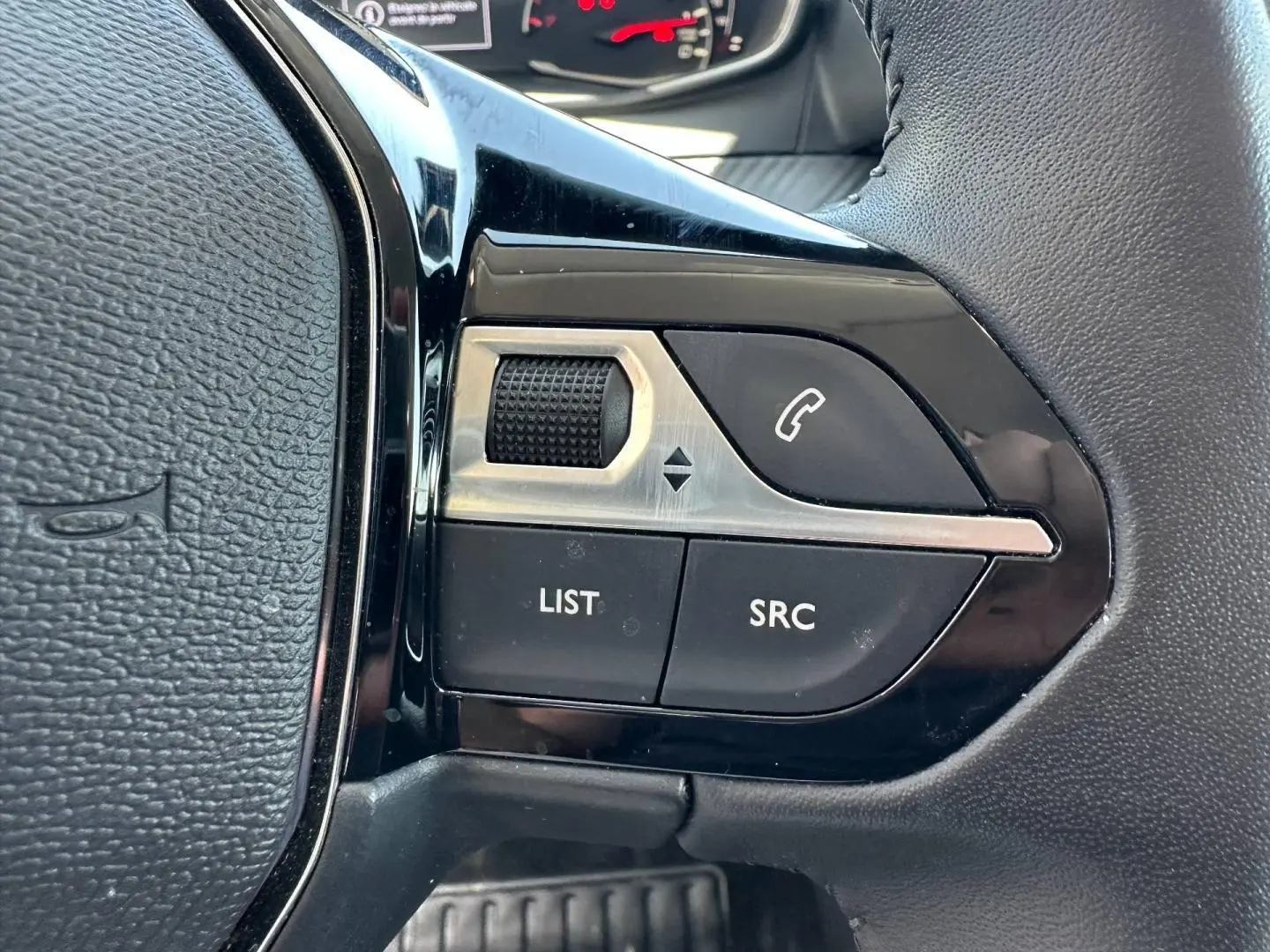 Gros plan sur les commandes audio au volant noir de la Peugeot 208 1.2 100ch Style, avec molette et boutons fonctionnels.