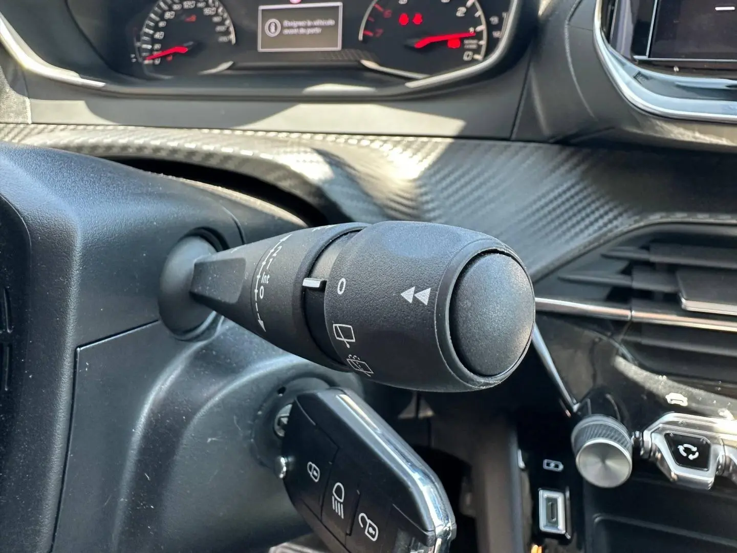 Gros plan sur la commande d’essuie-glace à gauche du volant dans l’habitacle d’une Peugeot 208 gris Artense.