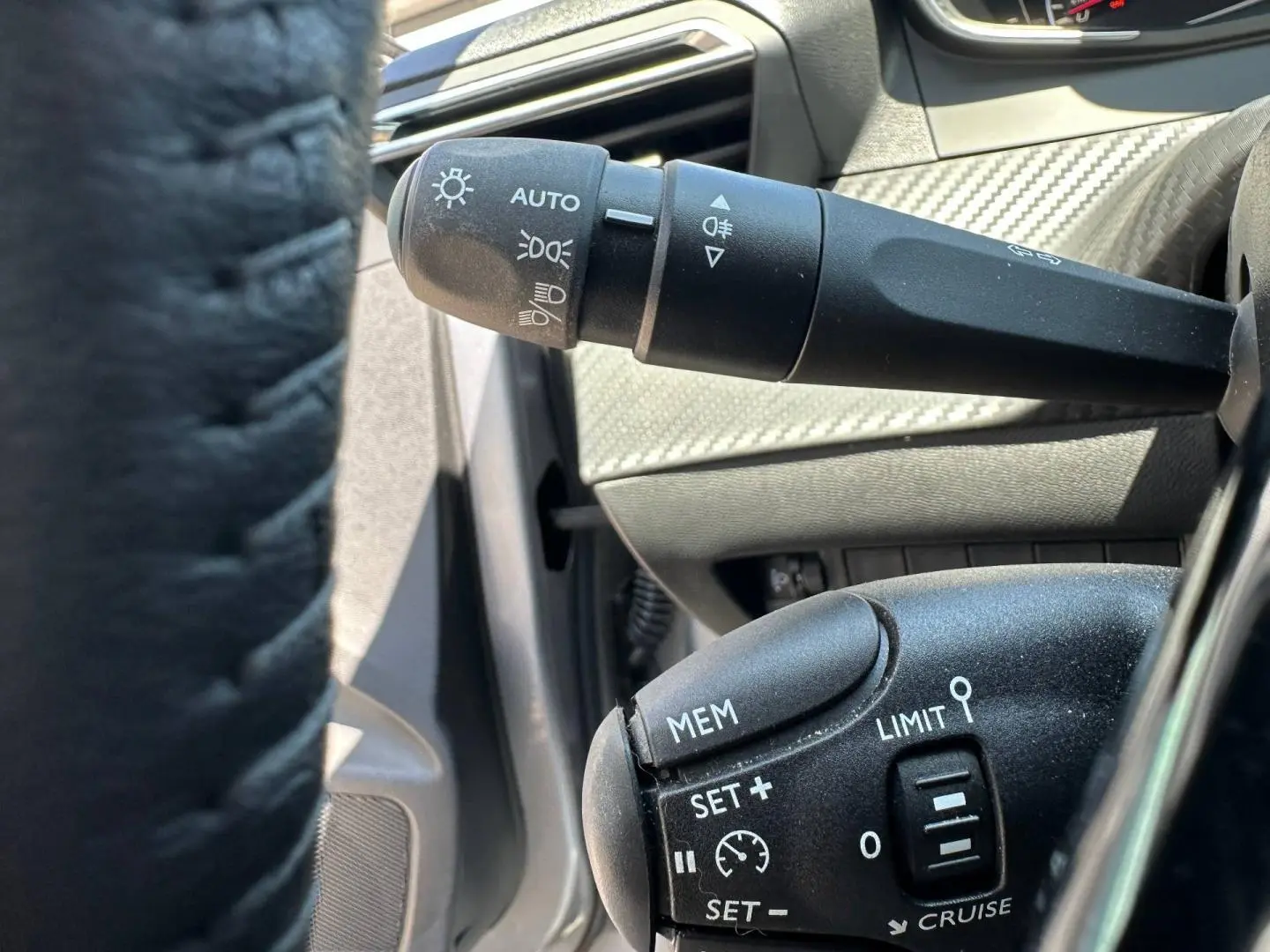 Gros plan sur les commandes de régulateur et feux au volant d’une Peugeot 208 gris Artense, intérieur noir.