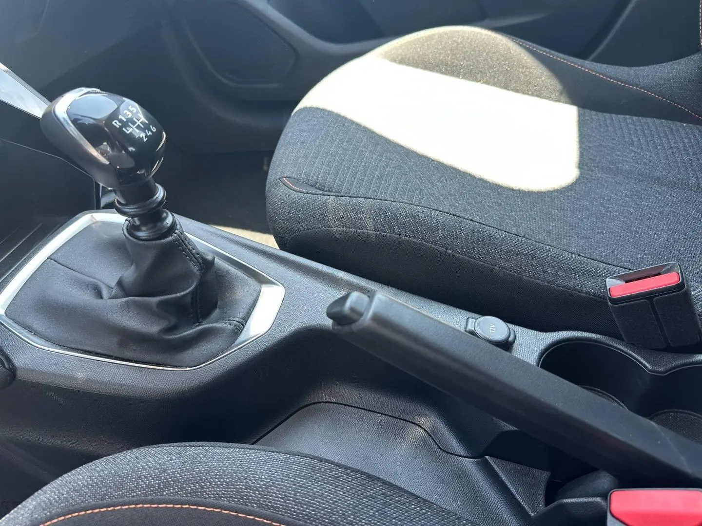 Vue intérieure rapprochée sur la console centrale d’une Peugeot 208 gris Artense avec levier de vitesse manuel et frein à main.