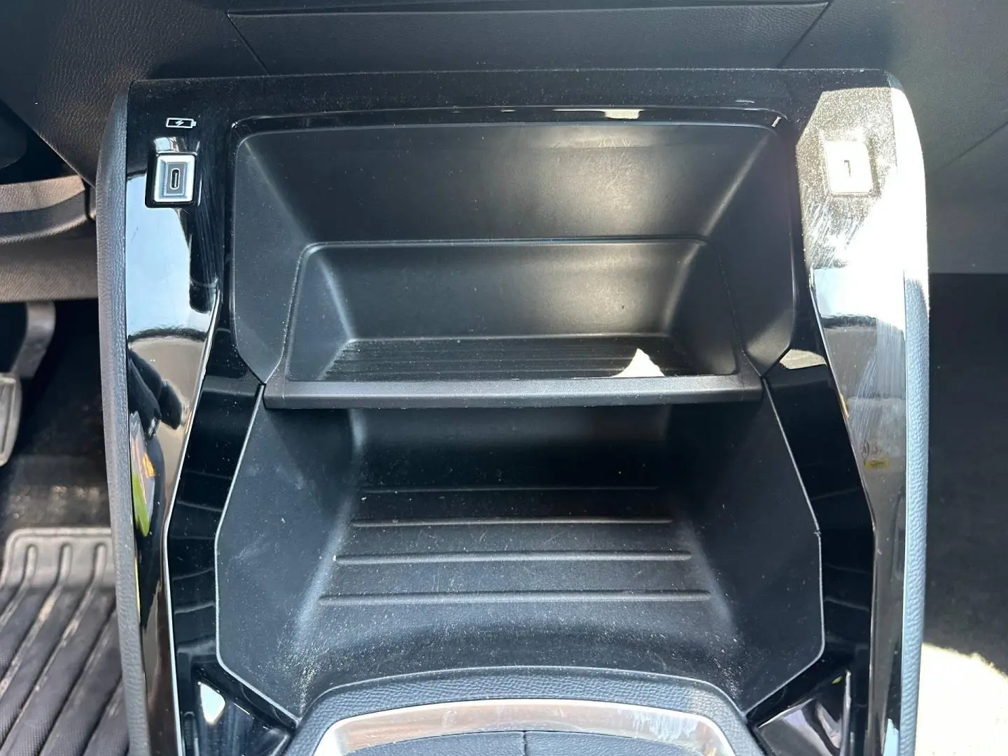 Gros plan sur le rangement central noir brillant de la Peugeot 208 1.2 100ch Style, avec ports USB visibles.