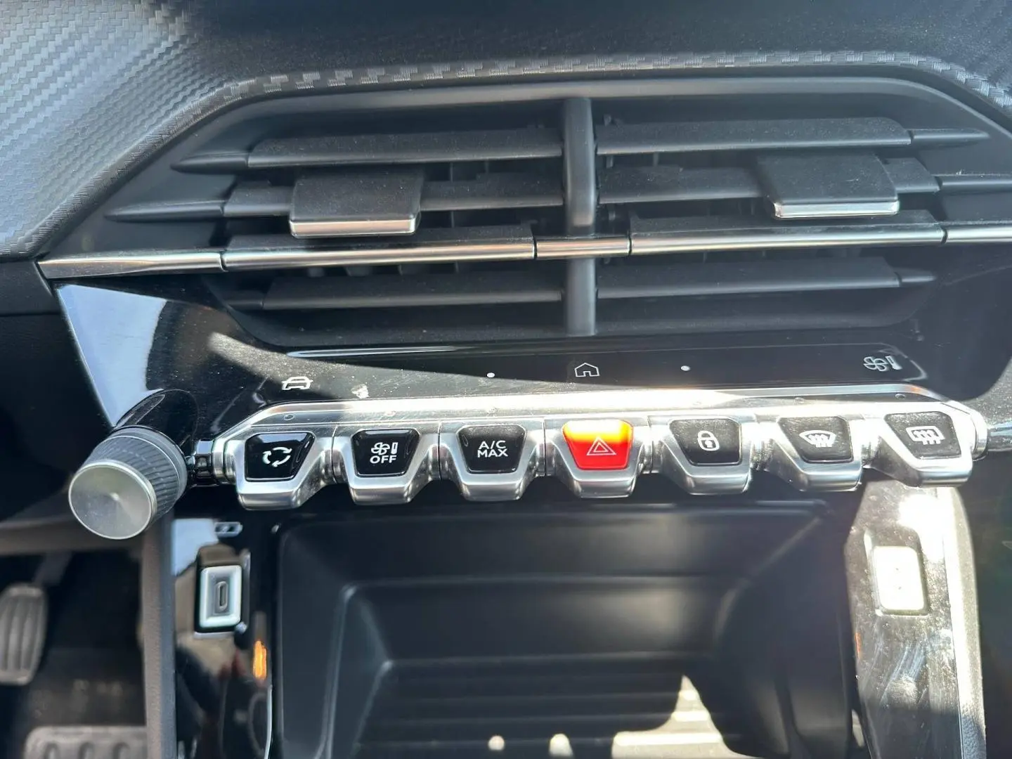 Vue rapprochée de la console centrale de la Peugeot 208 2025, boutons de commande argentés et noir avec bouton rouge d’alerte.