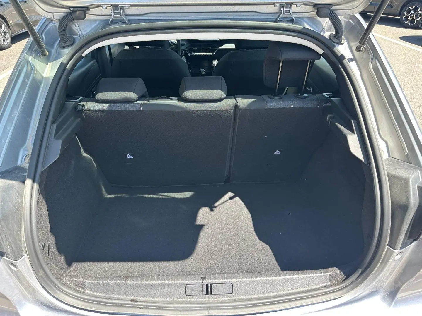 Coffre ouvert vu de l'arrière d'une Peugeot 208 gris Artense, banquette arrière en tissu noir avec surpiqûres visibles.