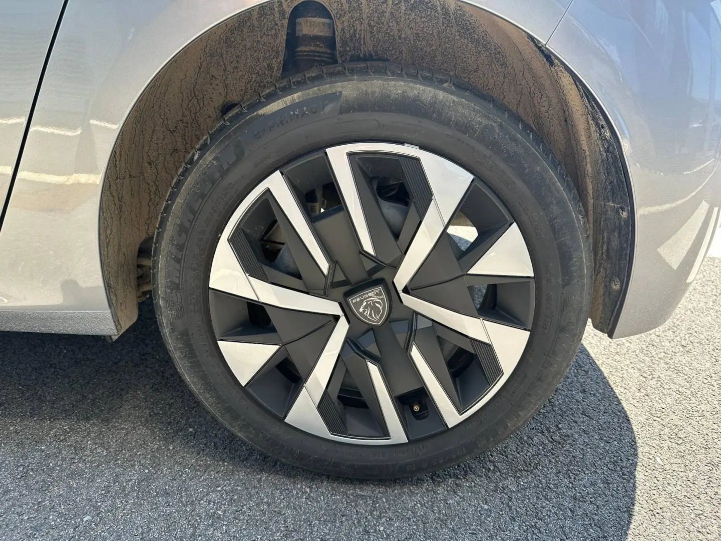 Gros plan sur la roue arrière droite d’une Peugeot 208 gris Artense avec jante au design géométrique noir et argent.