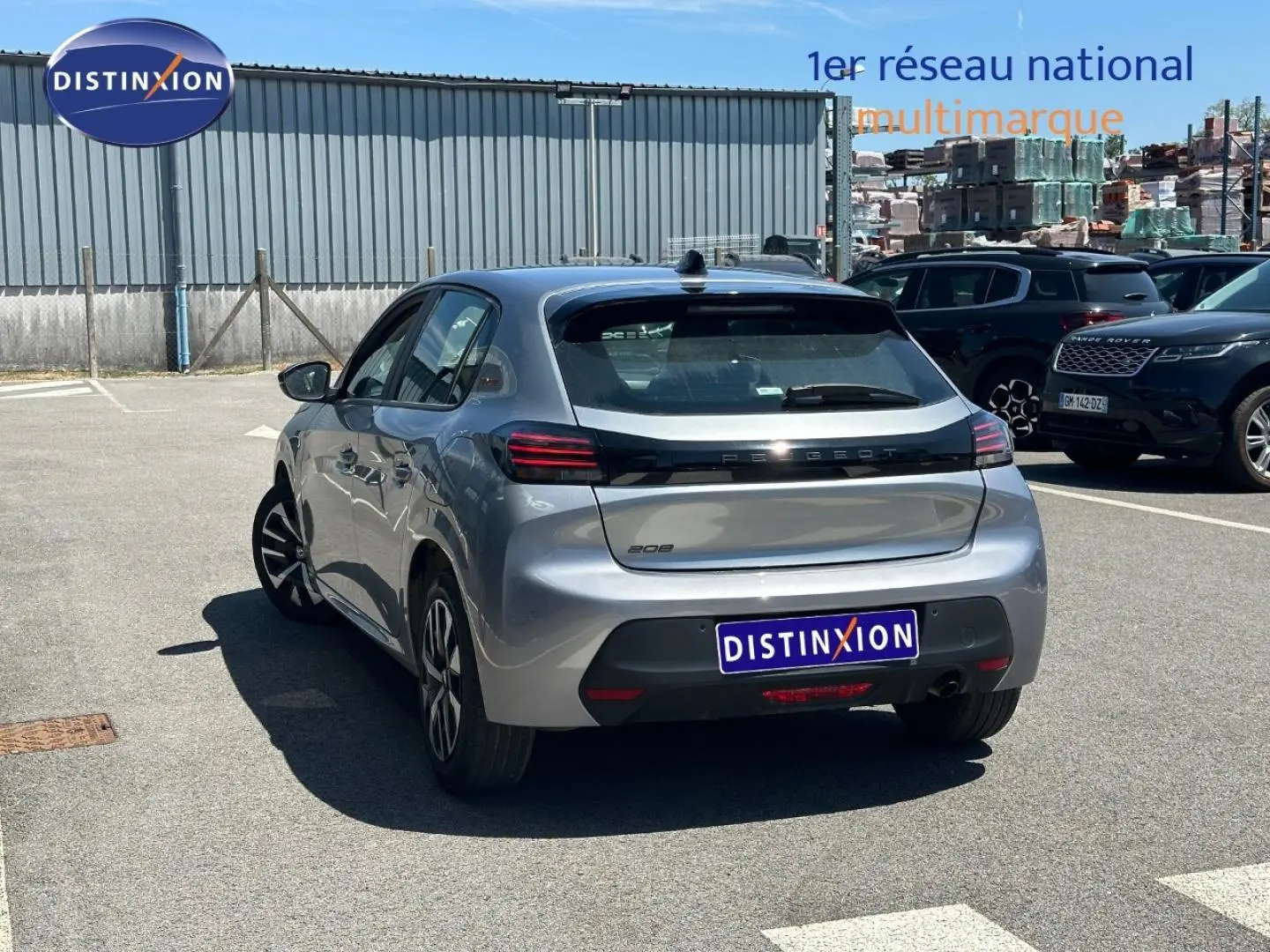 Vue 3/4 arrière droite d'une Peugeot 208 gris Artense garée sur un parking extérieur ensoleillé.