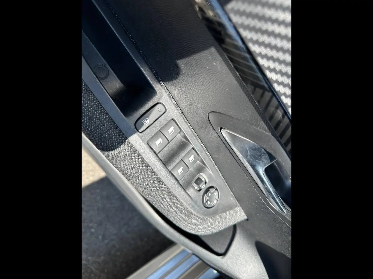 Détail de la porte avant gauche de la Peugeot 208 gris Artense, avec commandes des vitres et rétroviseurs électriques.
