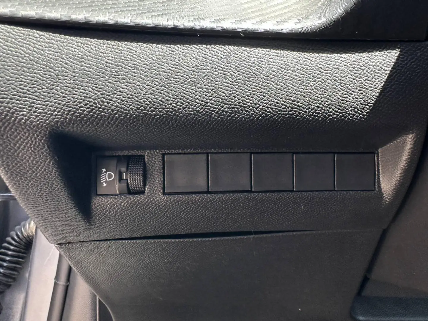 Détail du tableau de bord côté gauche avec réglage de hauteur des phares sur Peugeot 208 Gris Artense.