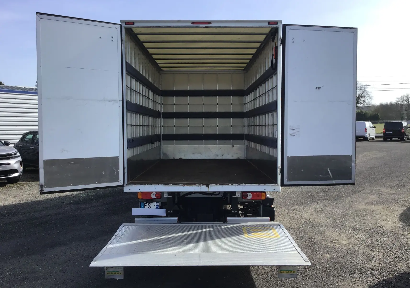 Vue arrière d’un Opel Movano blanc avec caisse ouverte et hayon déployé, montrant l’espace de chargement vide.