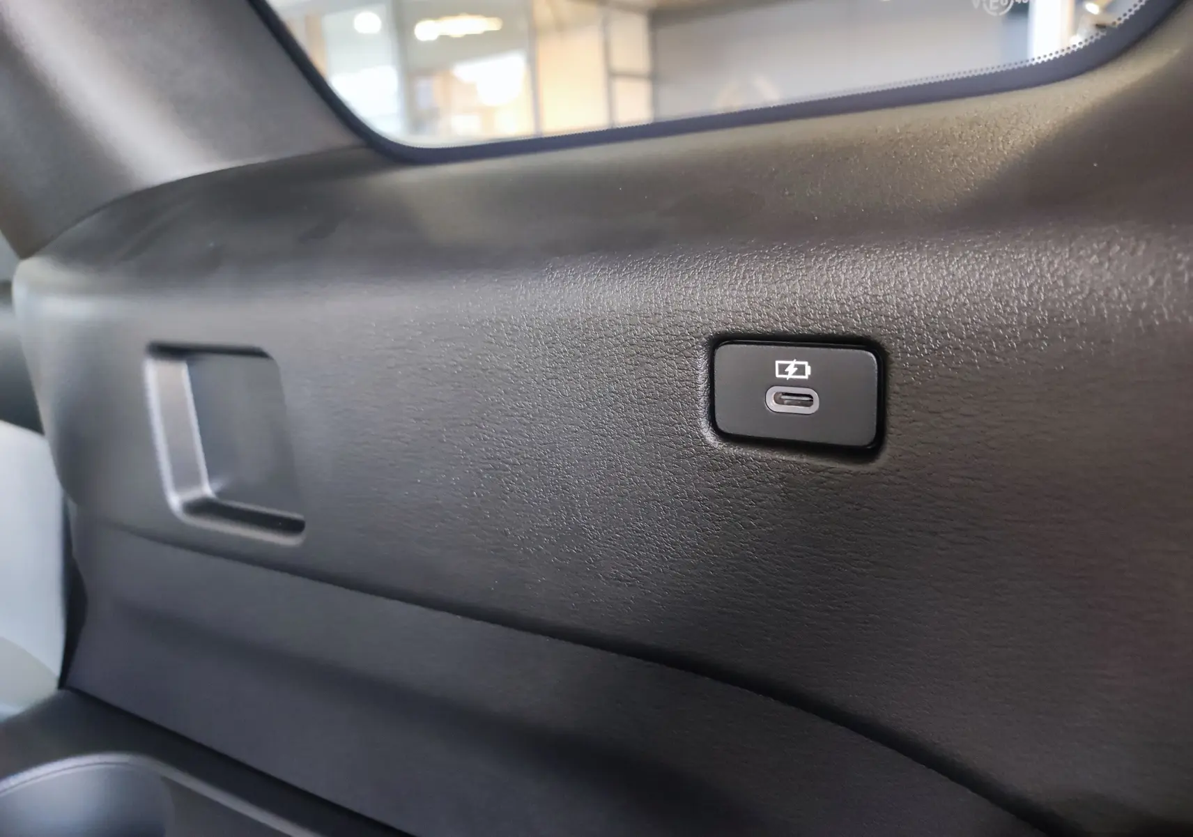 Bouton de recharge USB-C visible sur la garniture intérieure noire du coffre du Mazda CX-80 hybride rechargeable 2024.