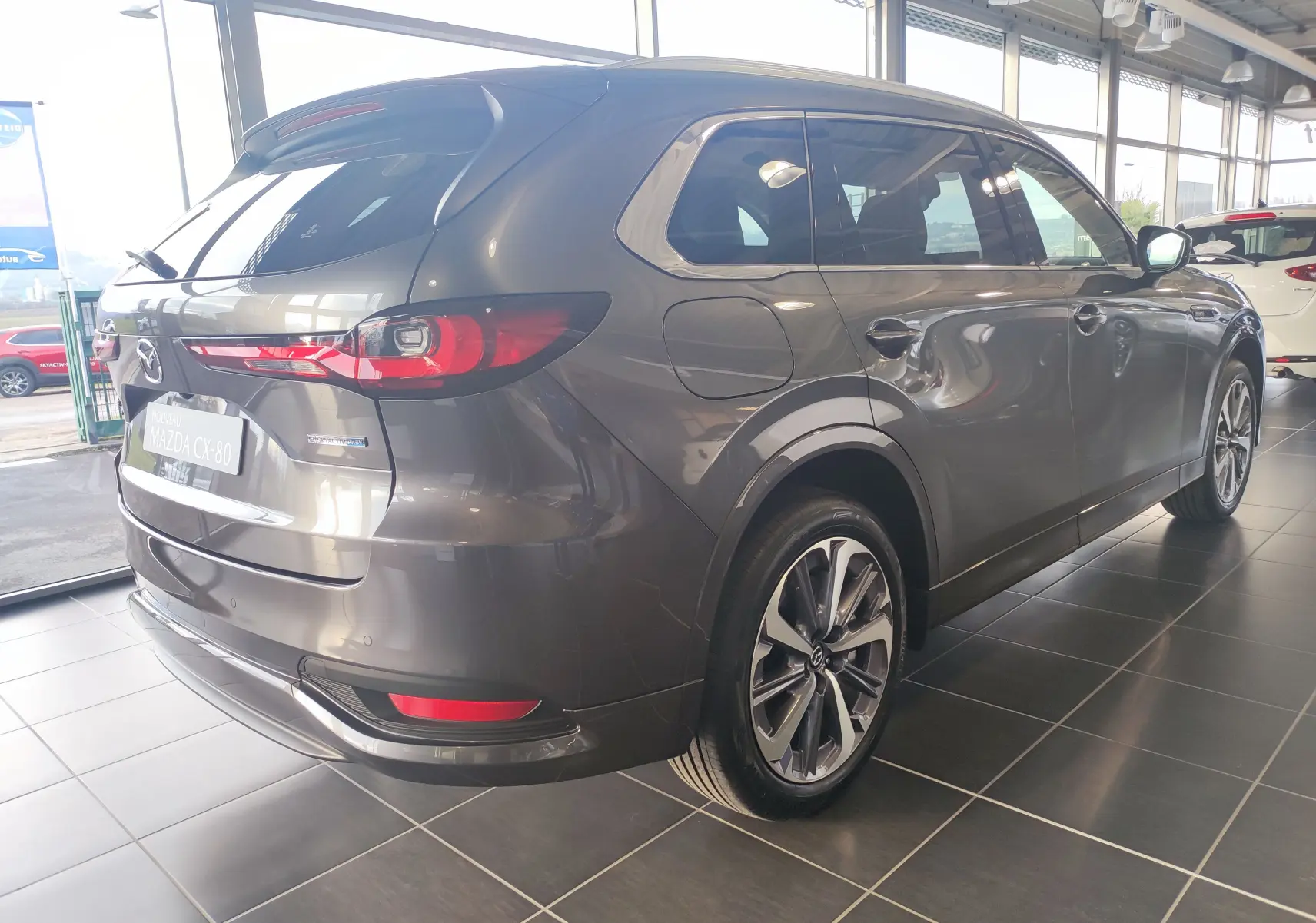 Vue 3/4 arrière droite du Mazda CX-80 gris foncé hybride rechargeable, avec feux arrière allongés et jantes alliage modernes.