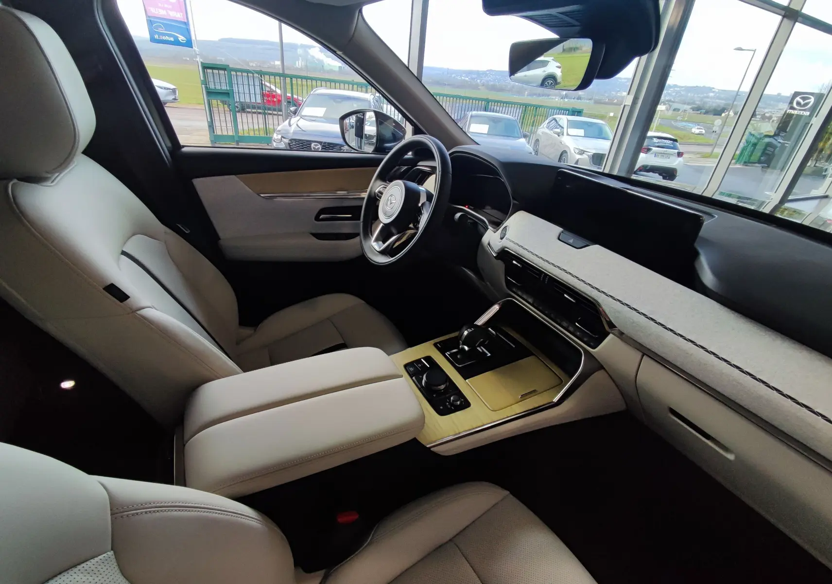 Intérieur clair du Mazda CX-80 2024, vue côté conducteur, avec tableau de bord moderne et console centrale boisée.