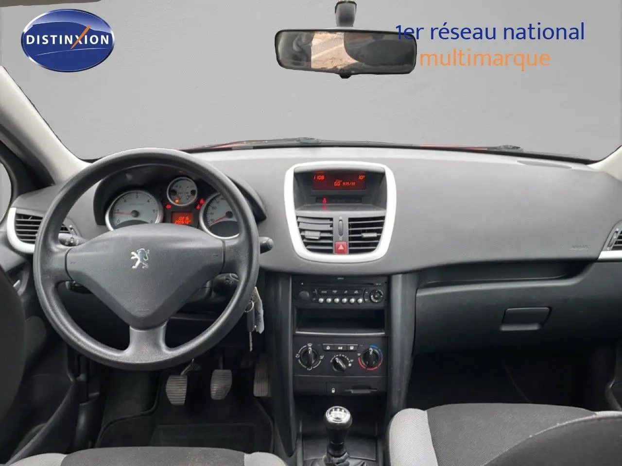 Vue intérieure avant du tableau de bord et volant noir d'une Peugeot 207 rouge métal de 2009 avec boîte manuelle.