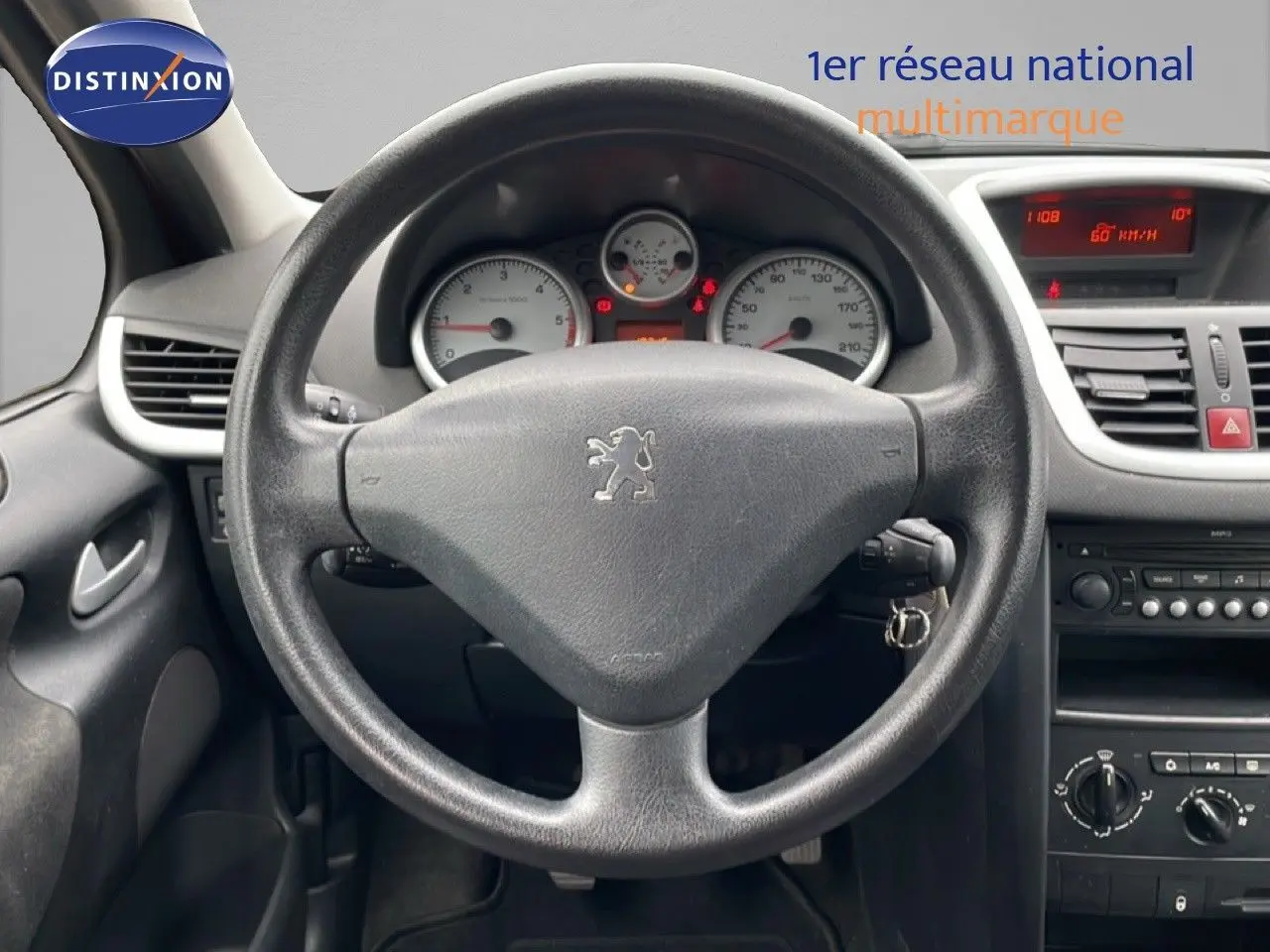 Vue intérieure centrée sur le volant noir de la Peugeot 207 HDI 70CH Trend de 2009 avec tableau de bord et commandes visibles.